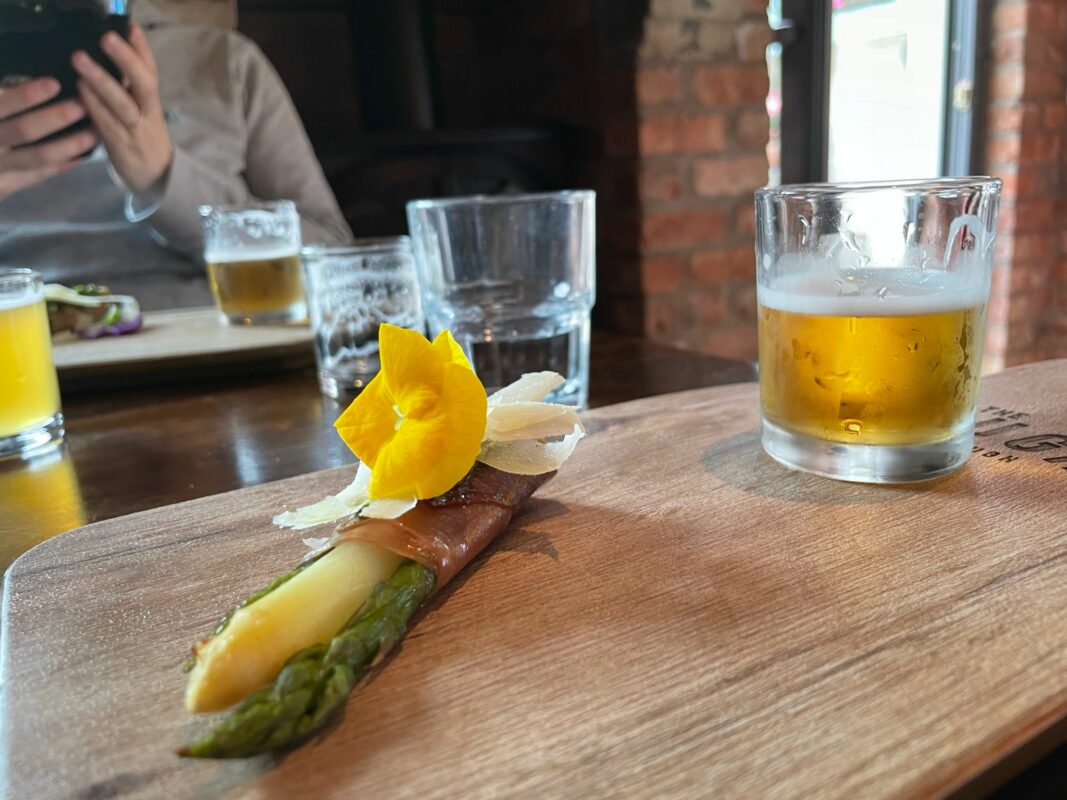 Aspagarus with a fresh flower displayed on a board with a beer sample